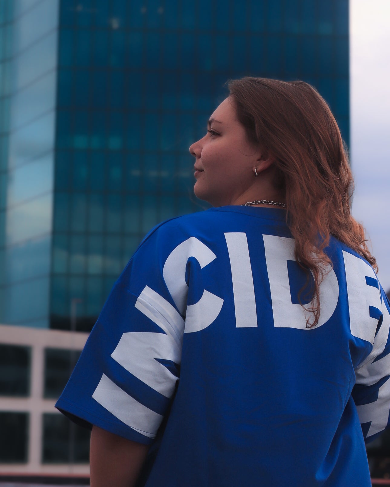 Person wearing a blue jersey with 'INCIDEN' text, standing in front of a modern building.
