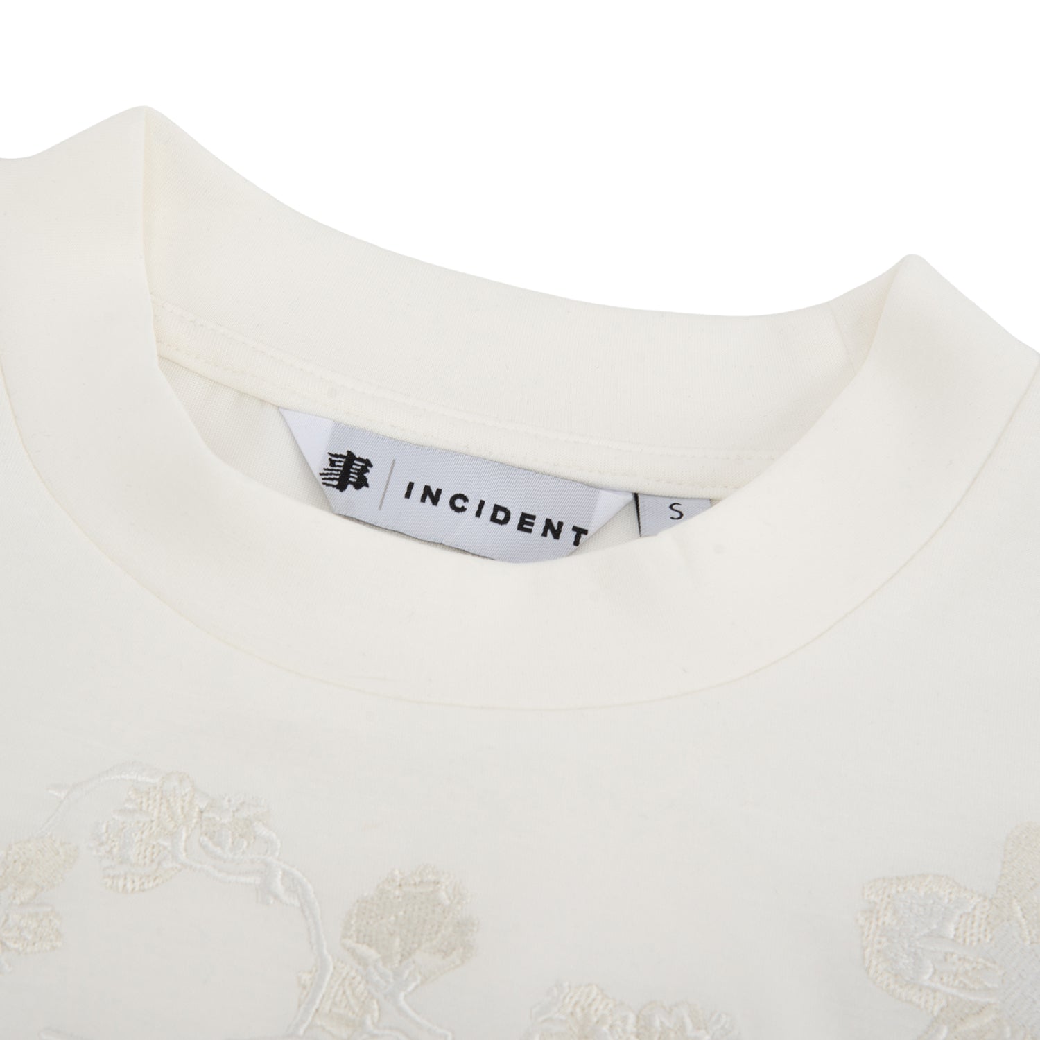 Close-up of a white garment with embroidery and a visible label on a white background
