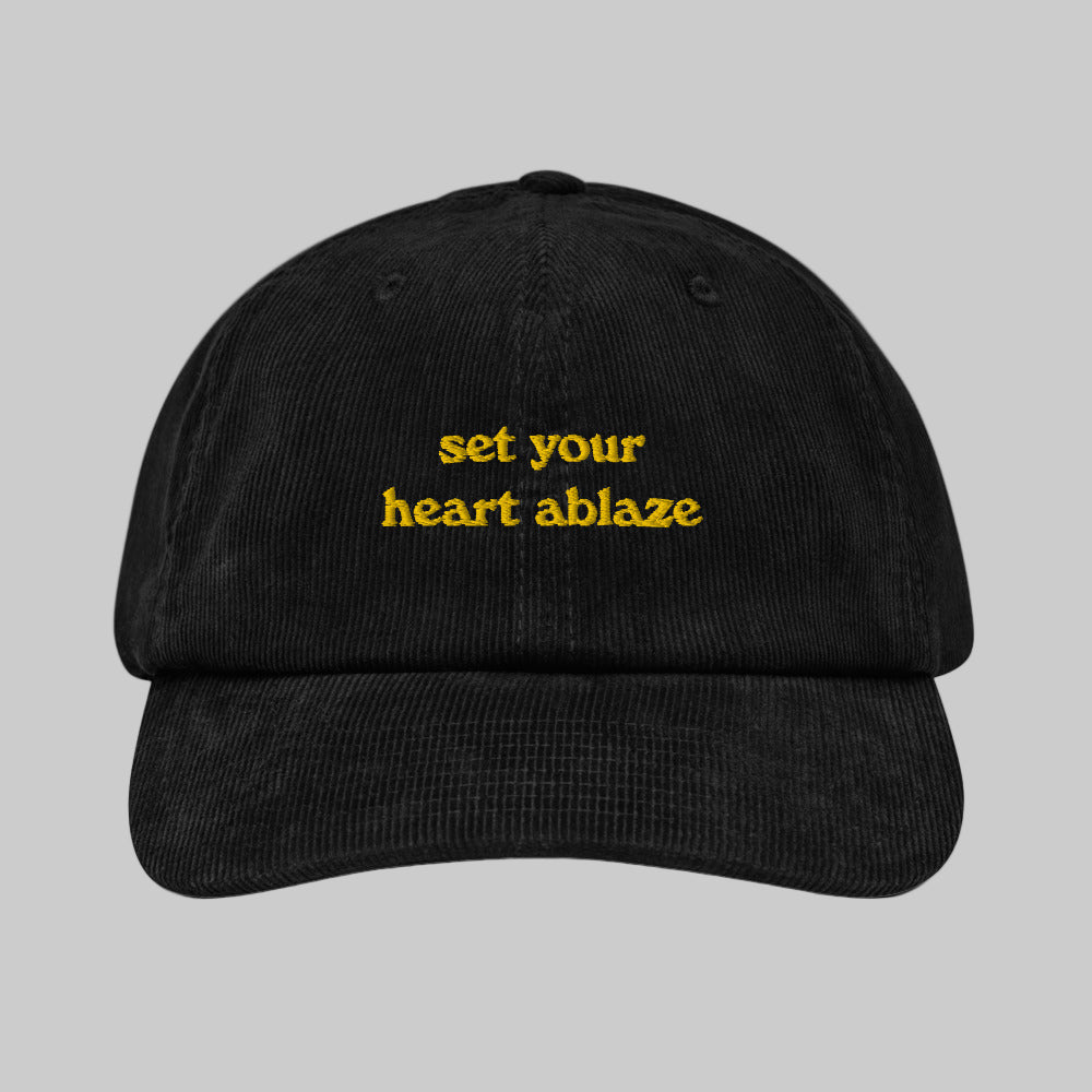 Black corduroy hat with the text 'set your heart ablaze' printed in yellow on the front.
