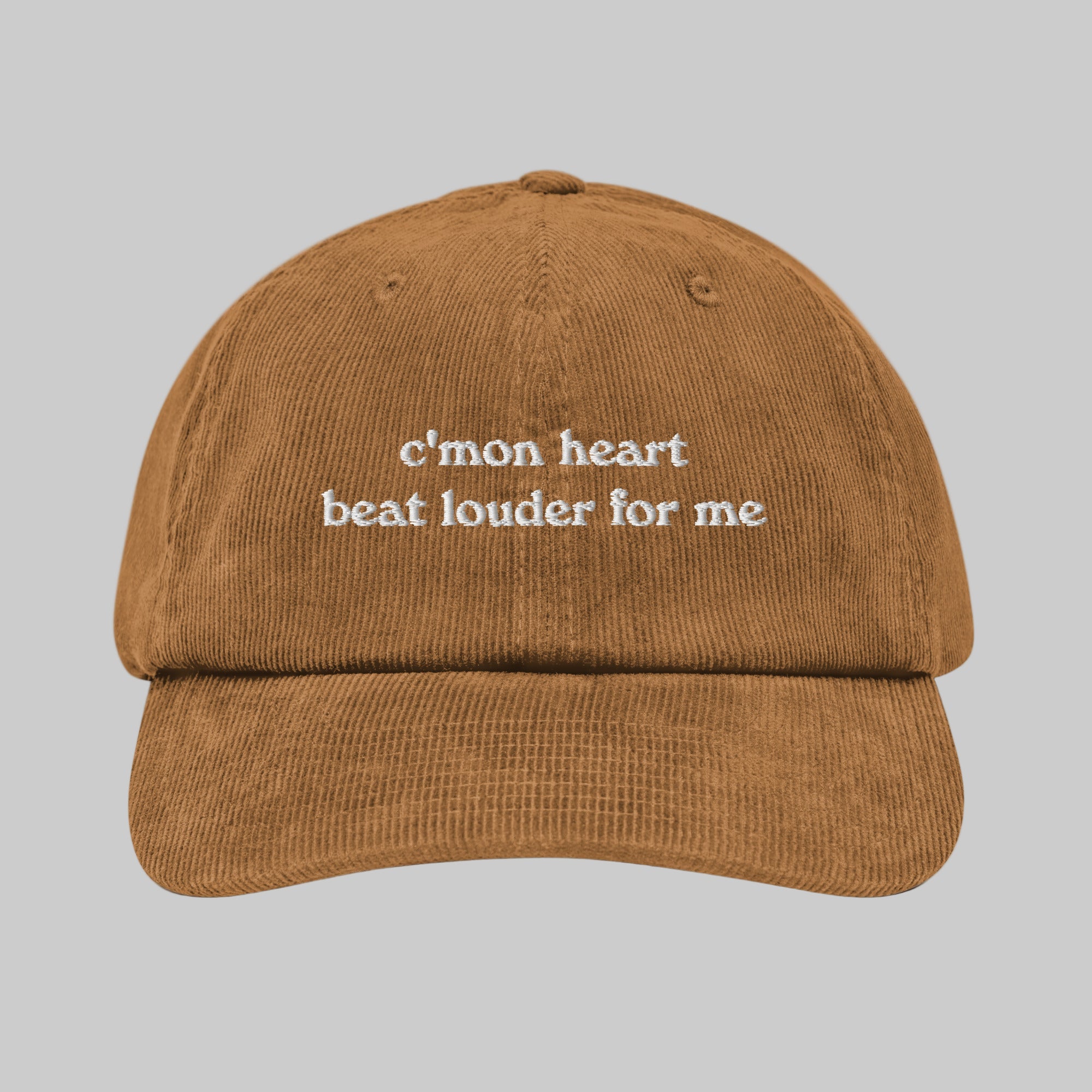 A brown corduroy baseball cap with the text 'c'mon heart beat louder for me' embroidered on the front.