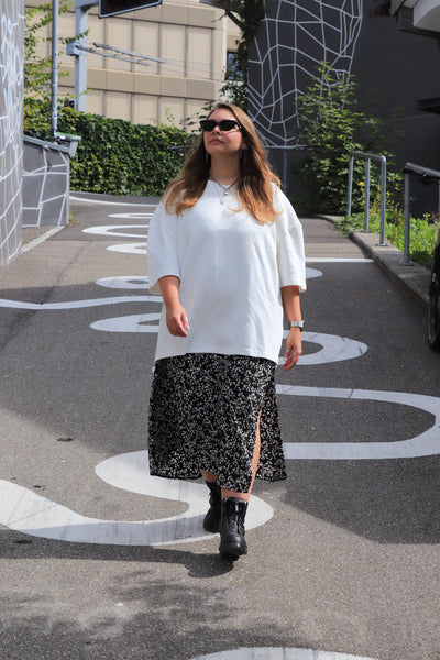 Woman in a white INCIDENT Pima Cotton T-Shirt and black patterned skirt walking on a street.